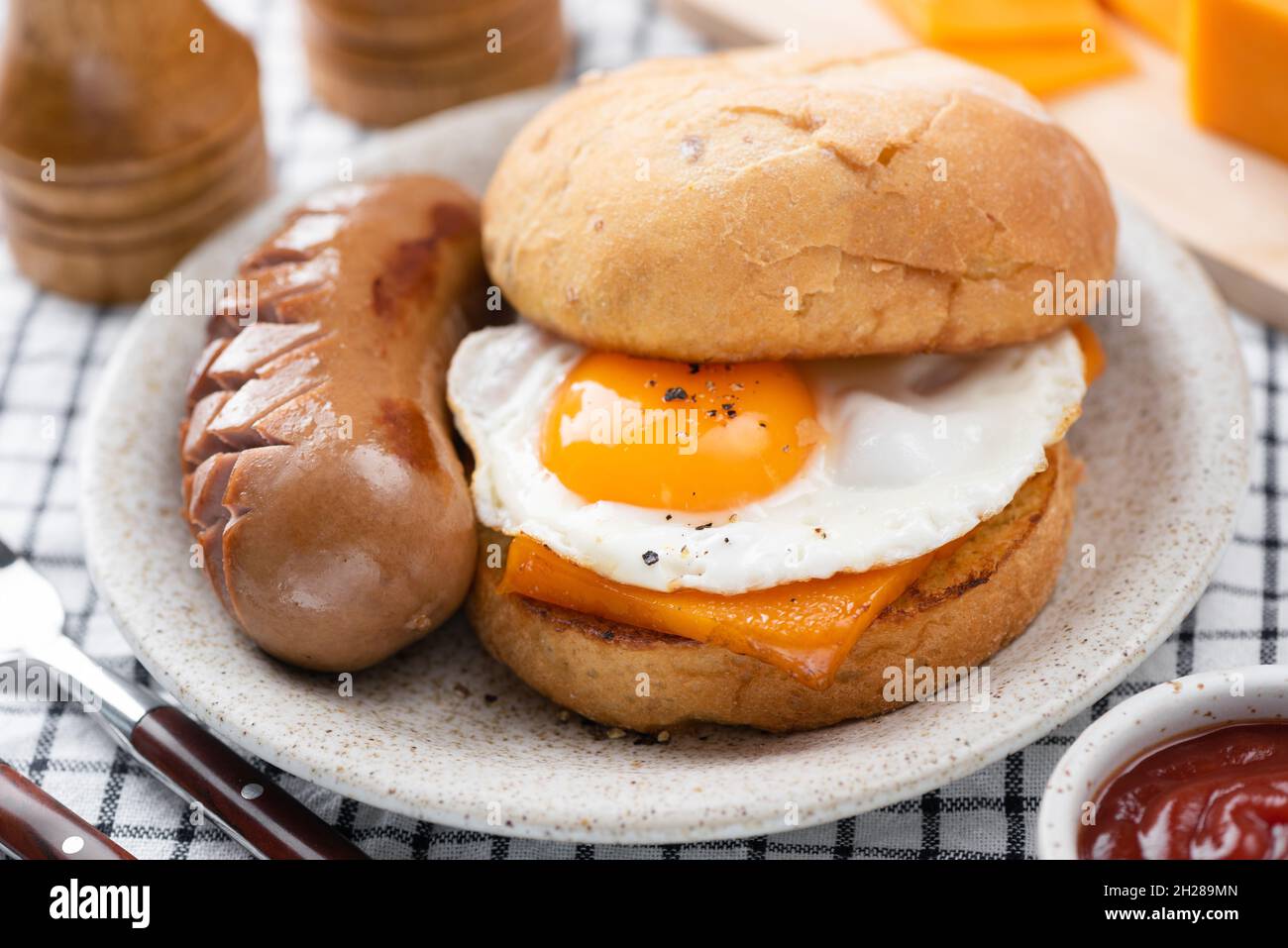 Amerikanisches Frühstückssandwich mit Wurst, Ei und Käse auf dem Teller, Nahaufnahme. Ungesunde Frühstückssnacks Stockfoto