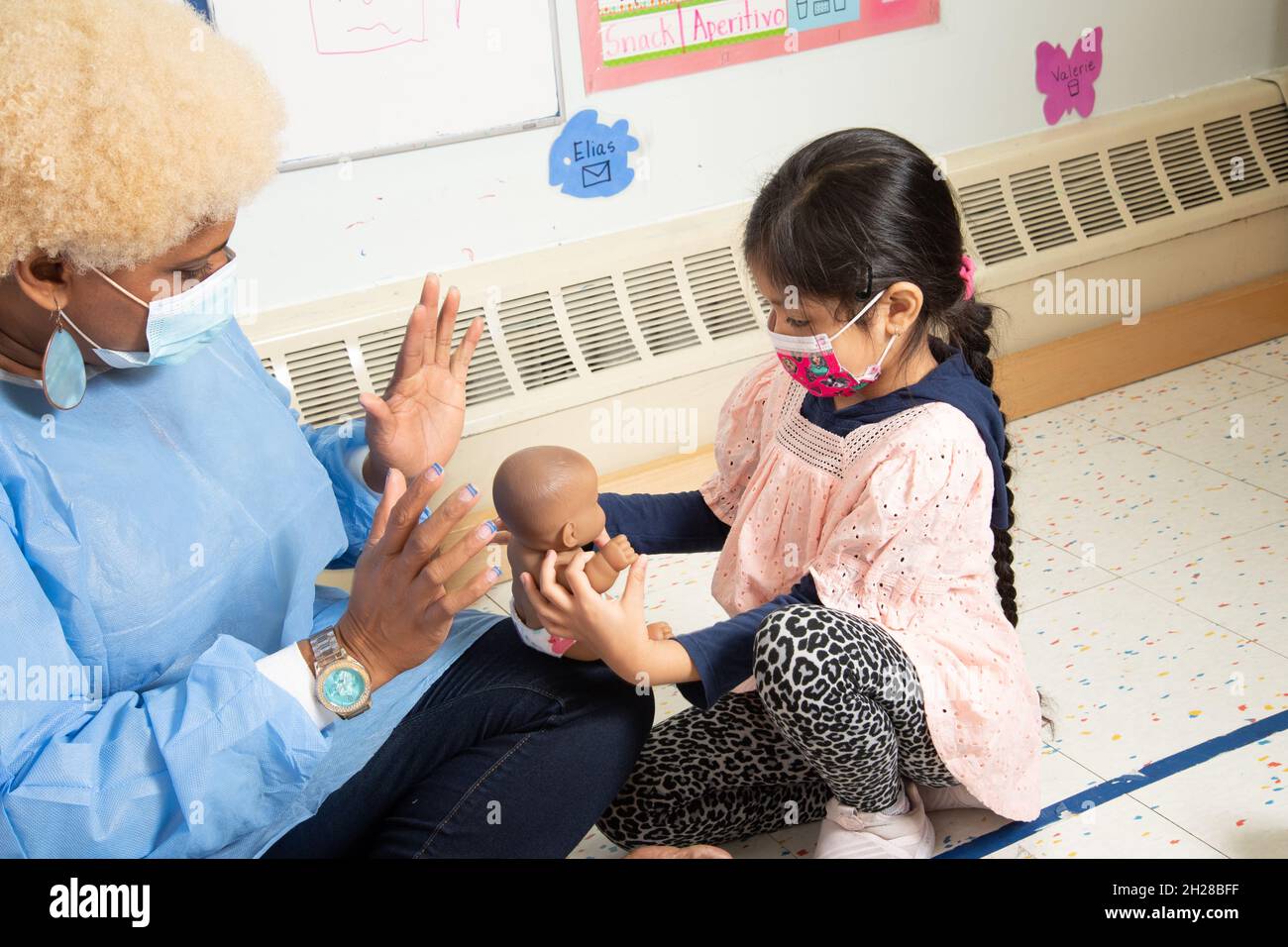 Bildung Preschool Mädchen im Alter von 4-5 Jahren mit Puppe spielen und interagieren mit dem Lehrer, beide tragen Gesichtsmasken, um gegen Covid-19 zu schützen Stockfoto