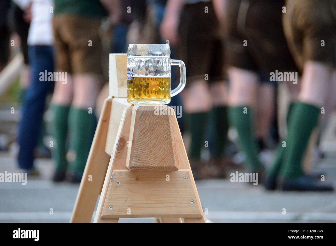 Ein Glas Bier steht beim Maibaumstellen auf einer Schrage, im Hintergrund die Beine der Mitwirkenden - Ein Glas Bier steht auf einem Hang, während die Stockfoto