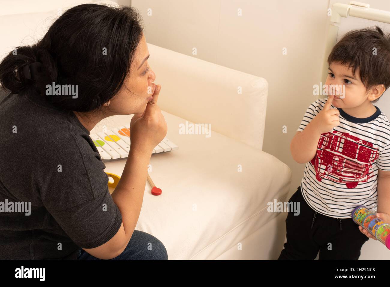 Mutter hält Finger an den Lippen und sagt shhh, während der 2-jährige Kleinkind sie imitiert Stockfoto