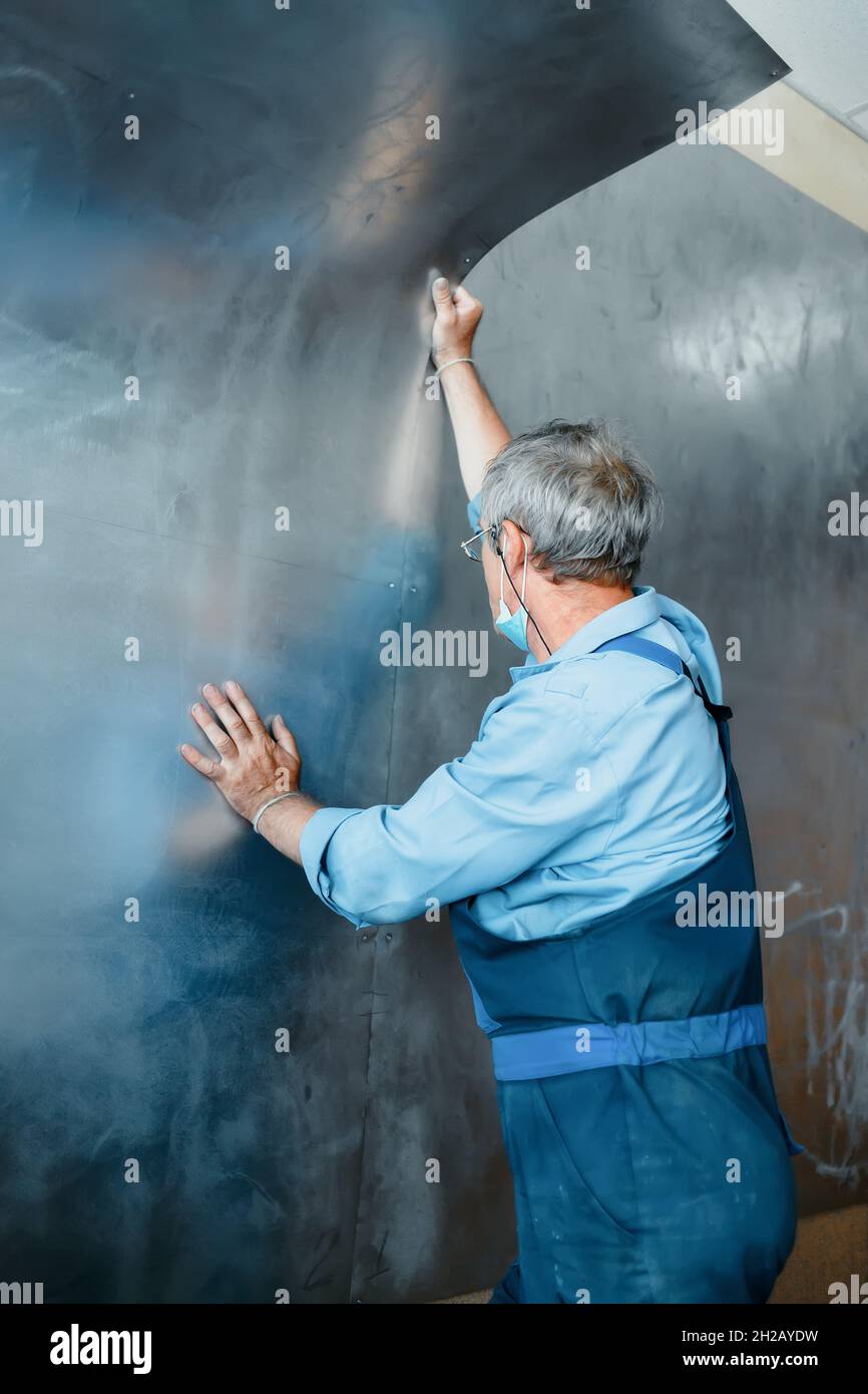Ein älterer Arbeiter umhüllt die Wände mit Metallblechen. Reale Szene der Arbeit.Konstruktion und Reparatur. Stockfoto