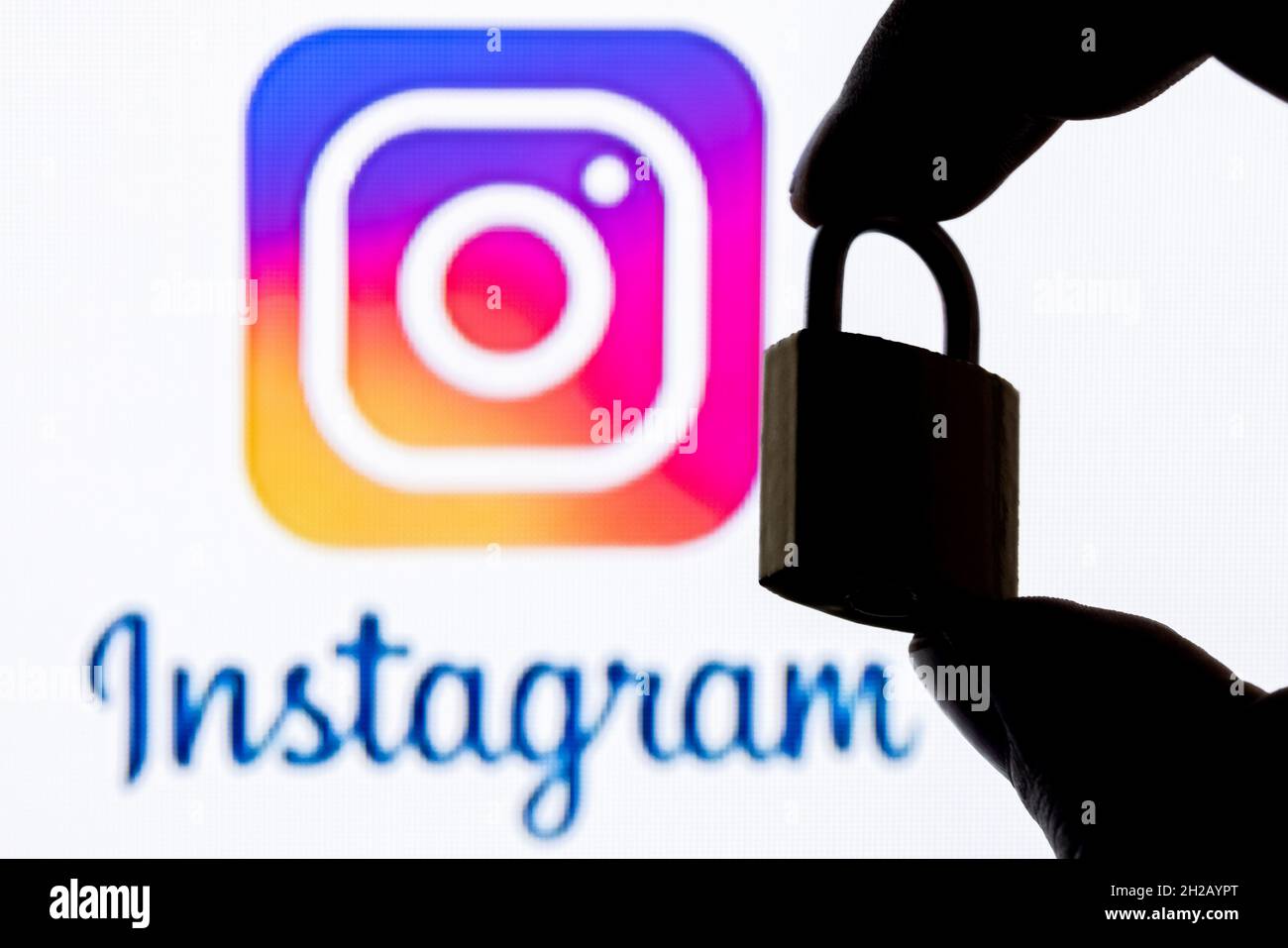 Finger halten eine geschlossene Sicherheitsverriegelung auf dem Hintergrund des Instagram Social Network-Logos. Das Konzept der Datensicherheit in Instagram. Stockfoto