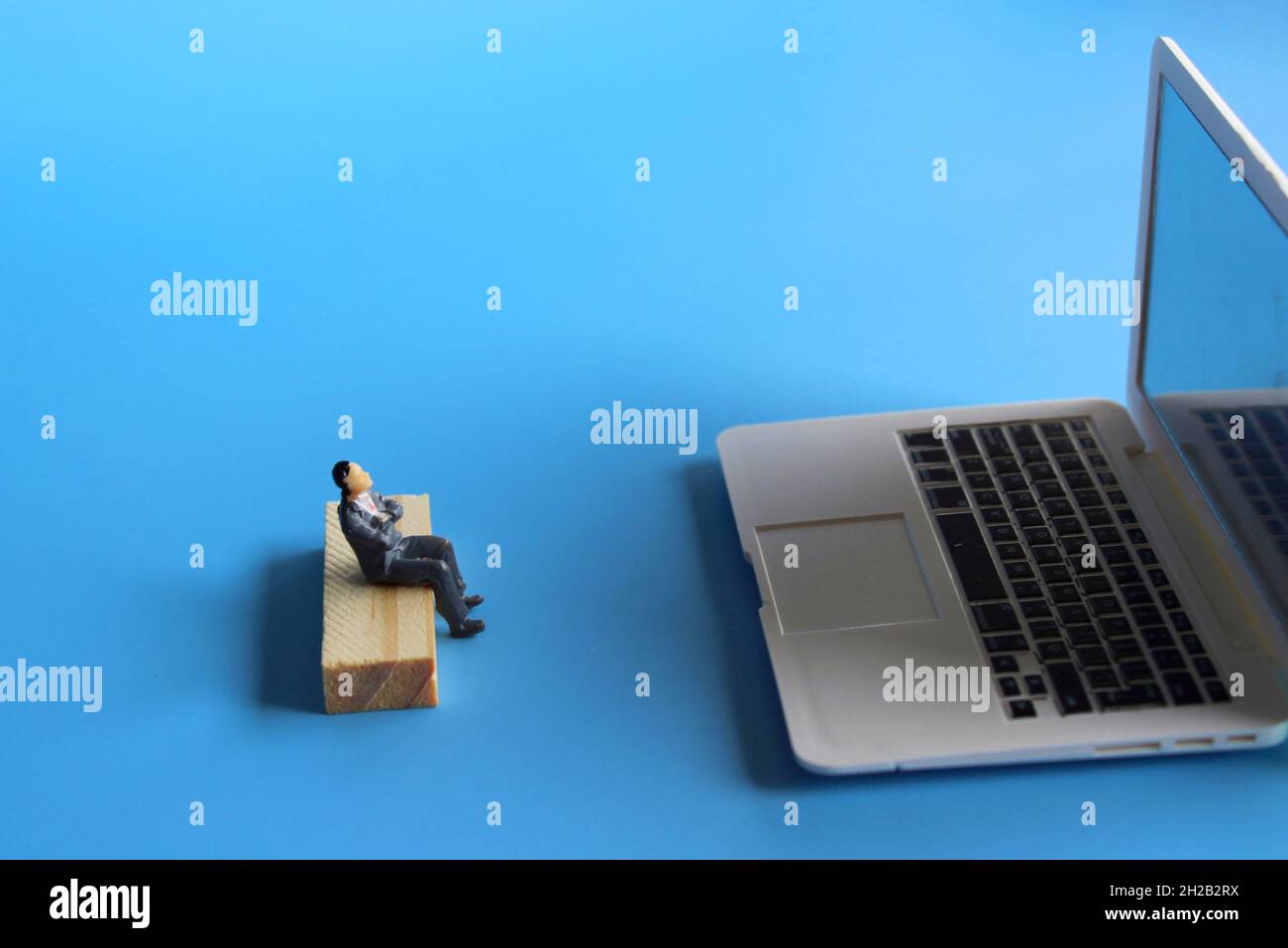 Online-Film-Streaming, Online-Meeting-Konzept. Miniatur-Mann sehen Film oder treffen auf Laptop. Blauer Hintergrund Stockfoto