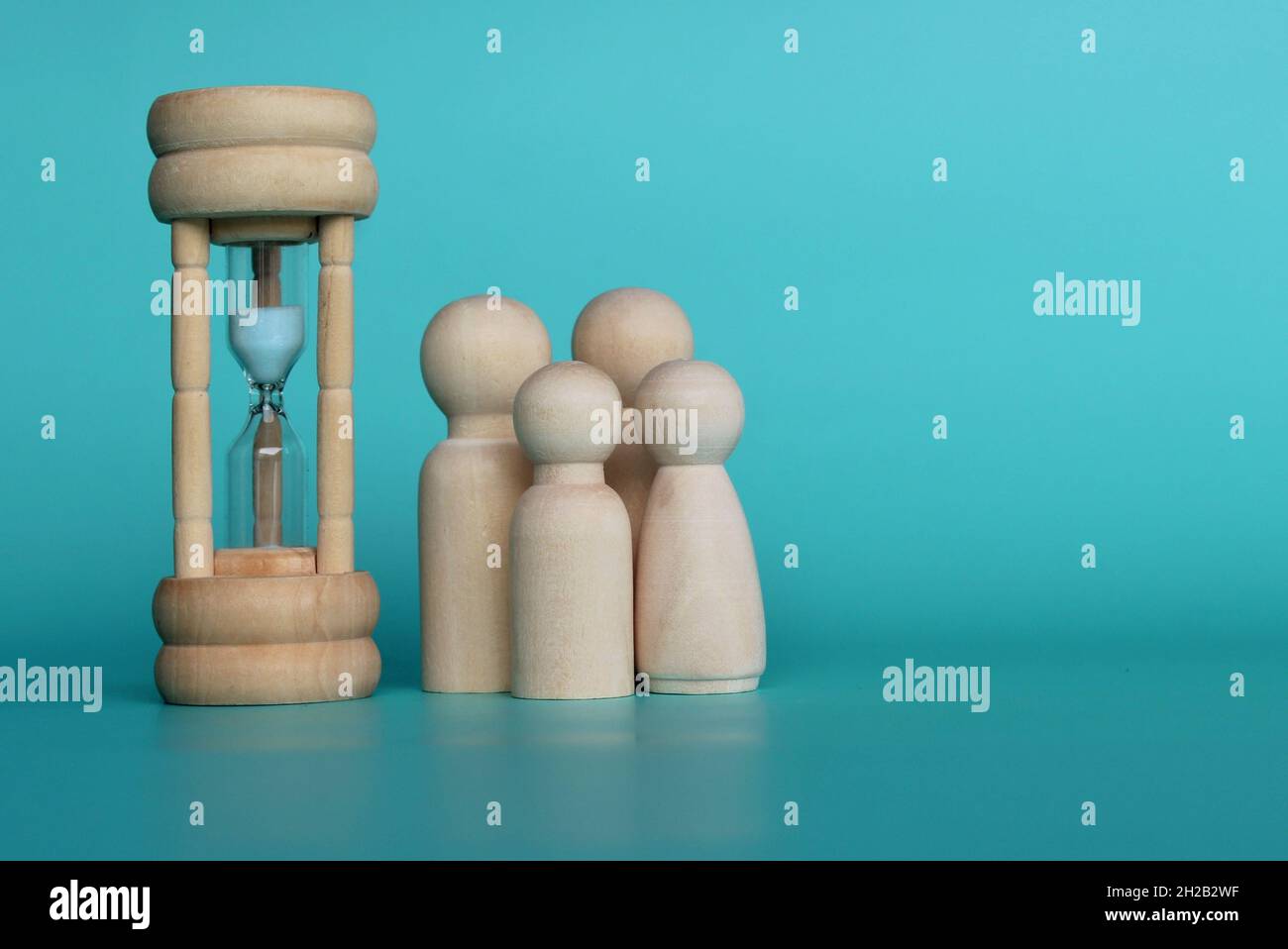 Zeit mit Familienkonzept. Holzpuppen und Sanduhr auf grünem Hintergrund mit Kopierraum Stockfoto