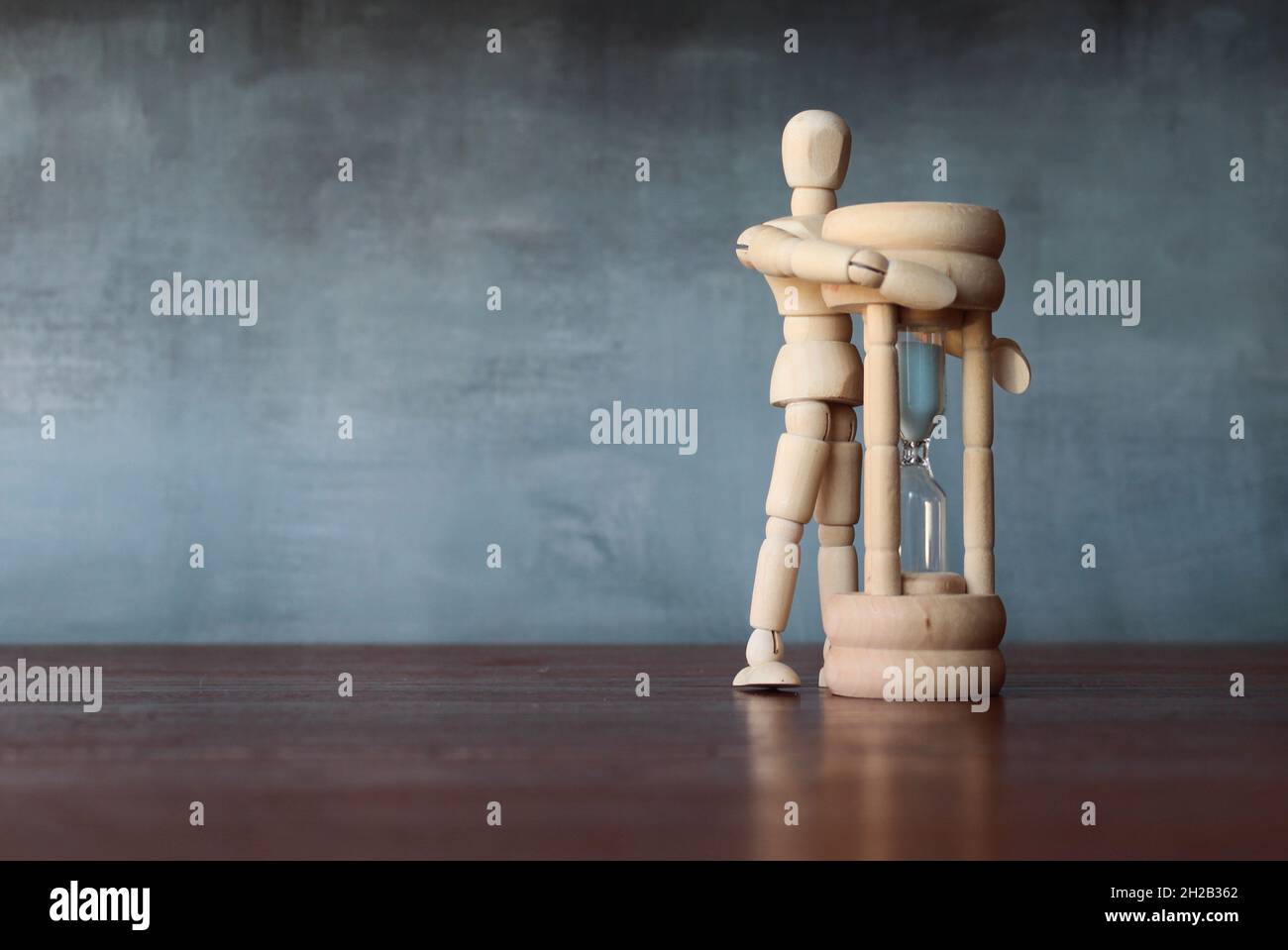 Zeitmanagement, aufhören zu verschwenden Zeit Konzept. Hölzerne menschliche Figur umarmt Sandglas. Platz für Text kopieren Stockfoto