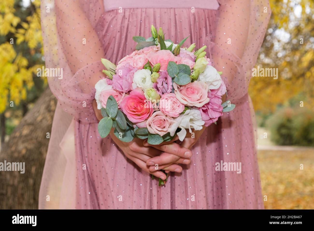 Die Braut in einem rosa Kleid hält einen Strauß rosa-weißer Rosen in der Herbstpark-Nahaufnahme. Stockfoto