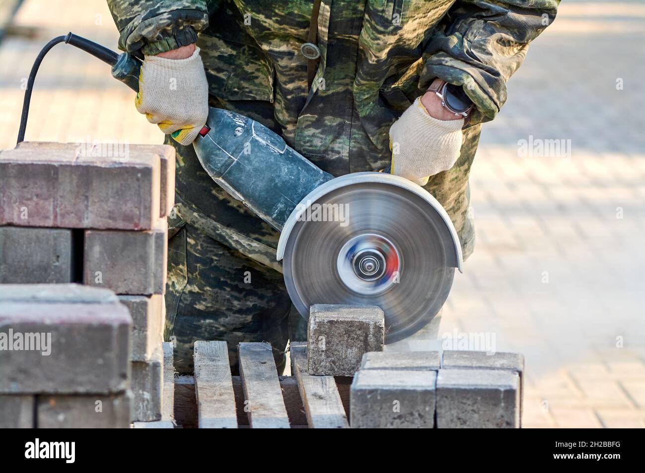 Ein Arbeiter mit einer Kreissäge schneidet in Nahaufnahme Pflasterplatten. Stockfoto