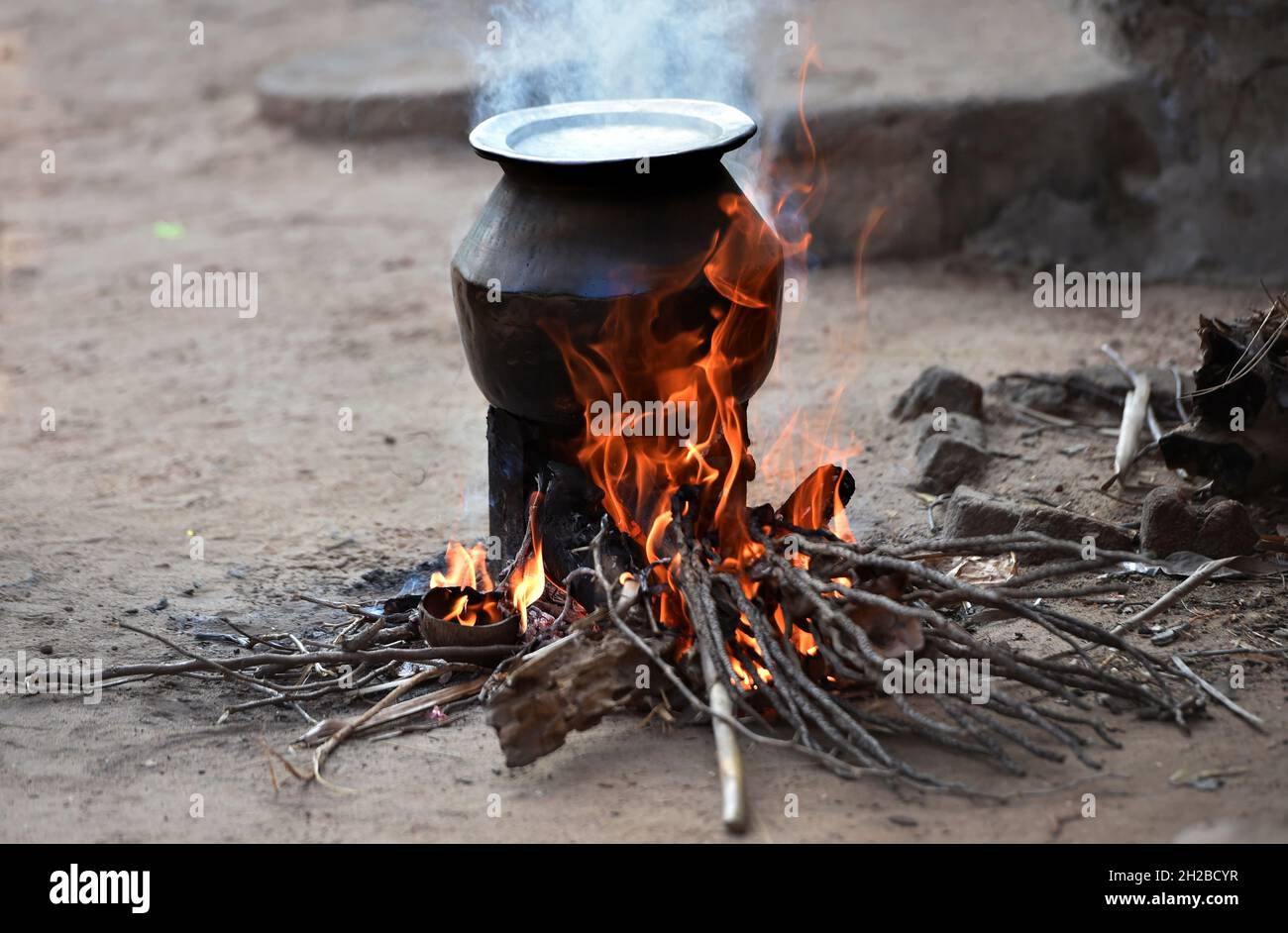 Offenes Feuer Kochen in einem indischen Dorf ein Aluminium-Utensil auf einem vorübergehend hergestellten Feuerofen. Ländliche Küche mit Bio-Holz Brennstoff zum Kochen. Desi Chulha Stockfoto
