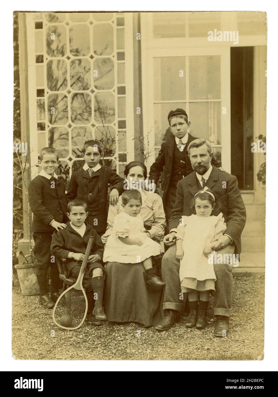 Originales edwardianisches Foto einer großen, attraktiven Familie, 6 Kinder, meist Jungen, die vor einem großen Haus sitzen. Die Mutter hat ein Baby oder Kleinkind auf dem Schoß, das in Mädchenkleidung gekleidet ist, aber ein Junge sein könnte, da kleine Kinder zu diesem Zeitpunkt gleich gekleidet waren. Wohlhabende Reiche sind gut für eine Familie. Großbritannien ca. 1908, Großbritannien Stockfoto