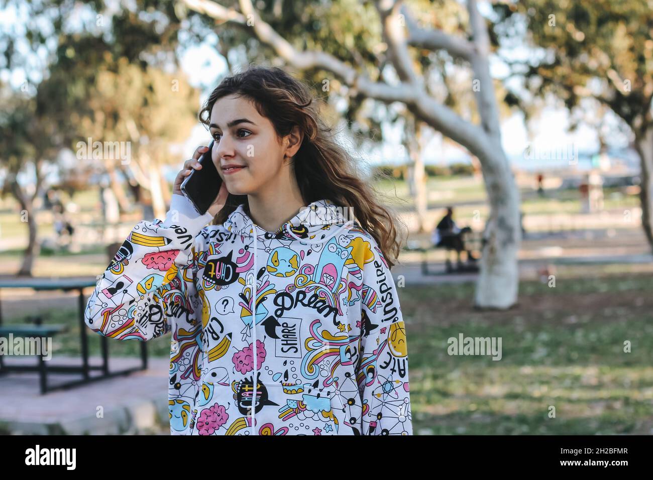 Nettes Teenager-Mädchen im Gespräch mit Freunden per Telefon. Ziemlich jugendlich draußen an den Bäumen Stockfoto