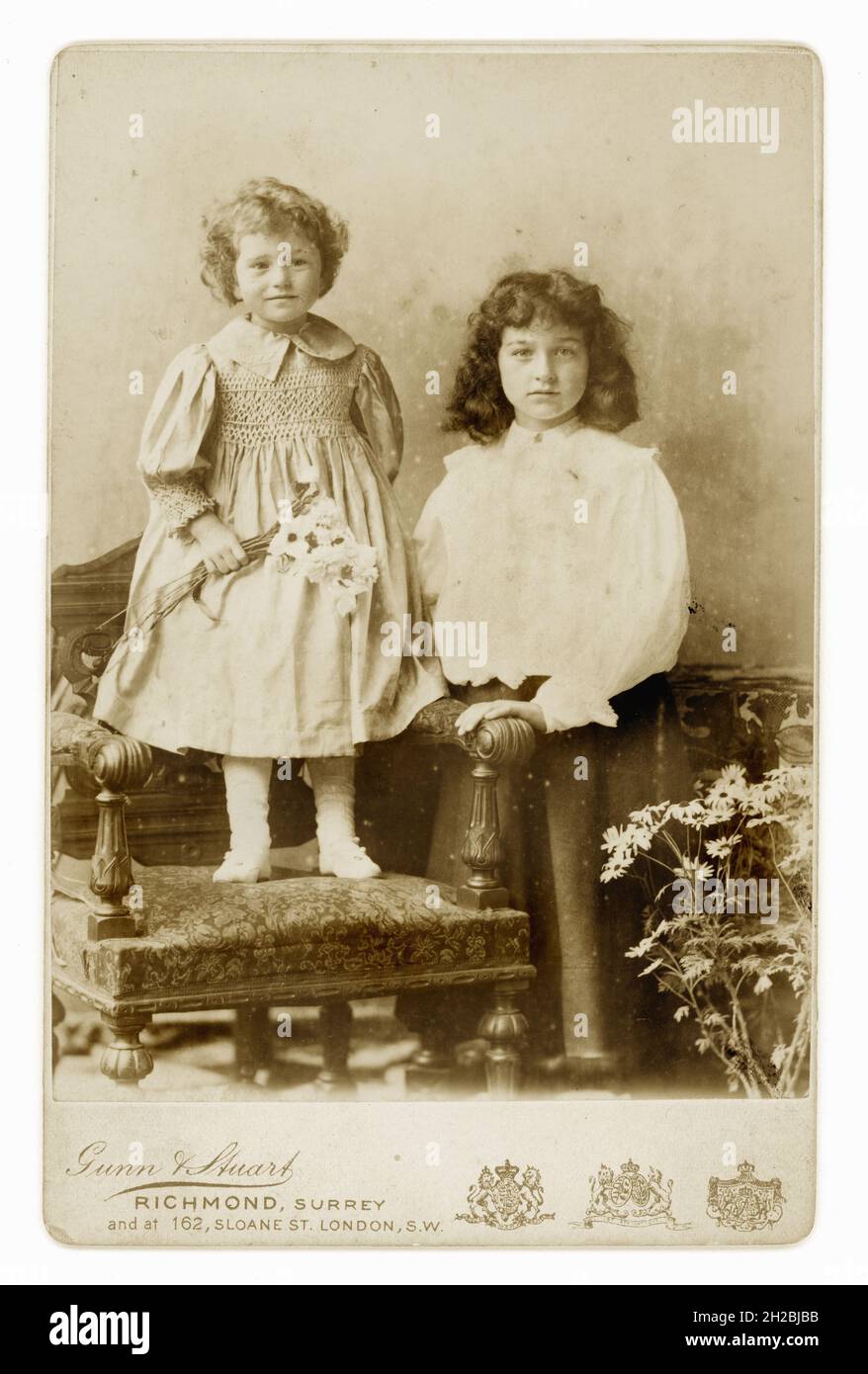 Originale viktorianische Schrankkarte aus den 1890er Jahren von zwei jungen viktorianischen Kindern, gesmokte Details auf dem jüngsten Kinderkleid, aus dem Atelier von Gunn & Stuart, Richmond, Surrey, Großbritannien um 1896 oder 1897. Stockfoto