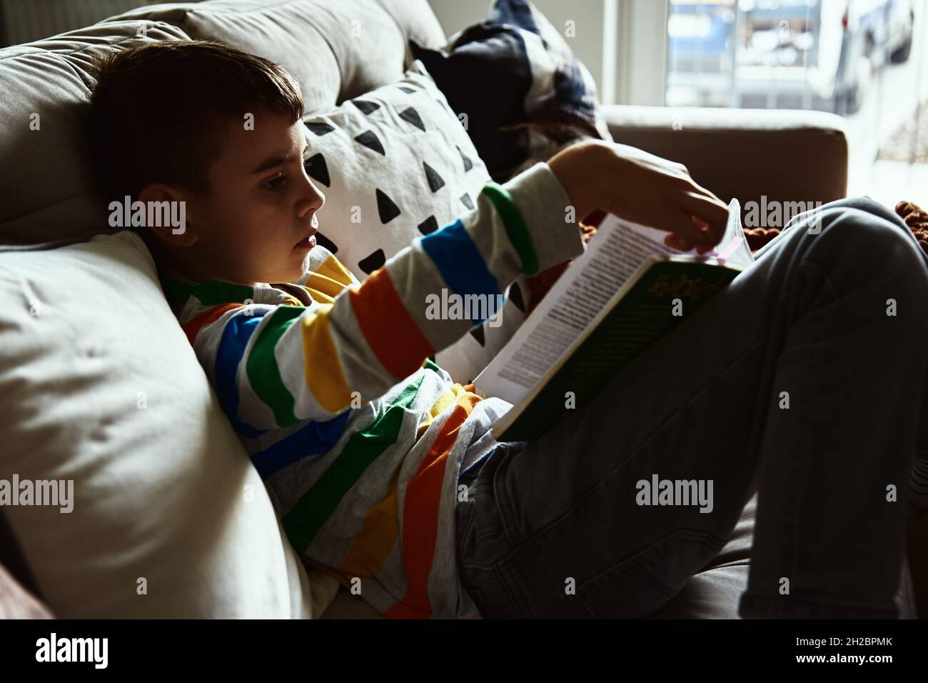 Kleiner Junge liest Buch auf dem Sofa zu Hause Stockfoto