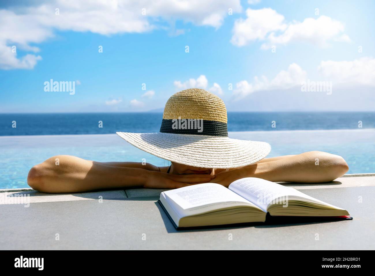 Frau versteckt sich unter Strohhut und ruht im unendlichen Pool. Entspannender Sommerurlaub im Resort Stockfoto