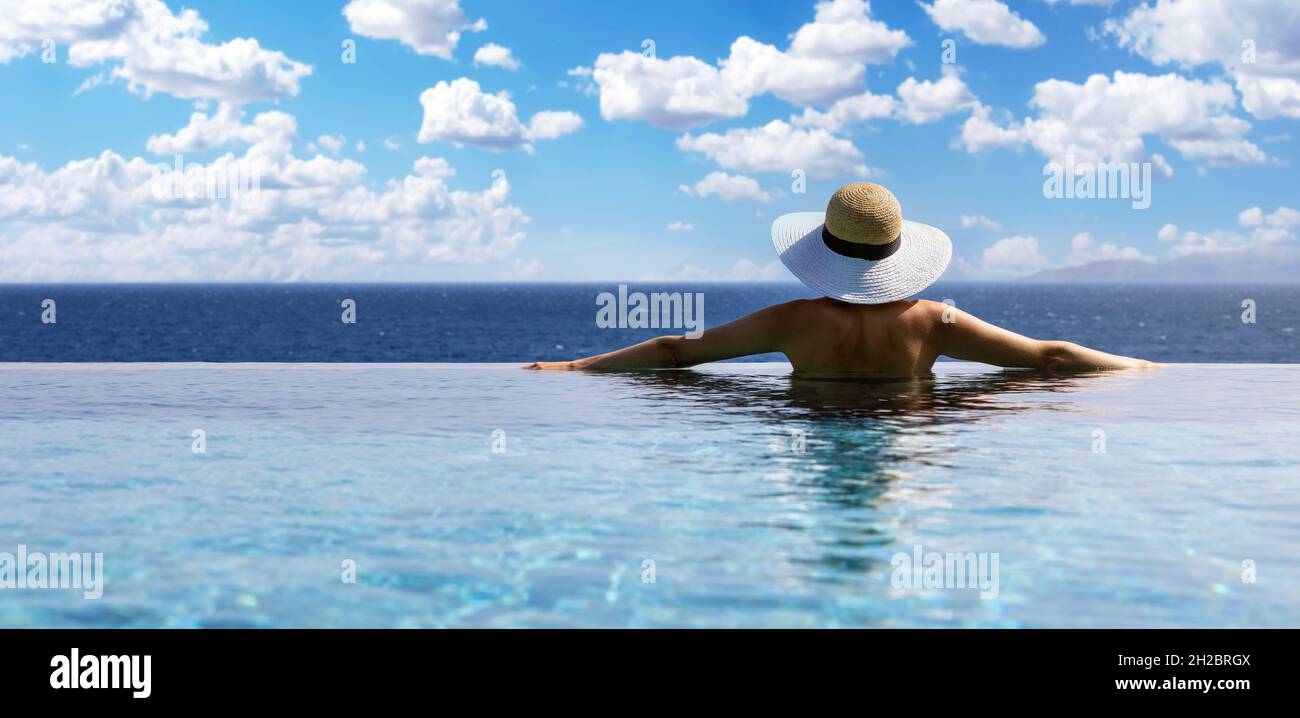 Frau mit Strohhut im Unendlichen Swimmingpool mit Meerblick im Luxus-Resort. Sommerurlaub Hintergrund. Copy space Stockfoto