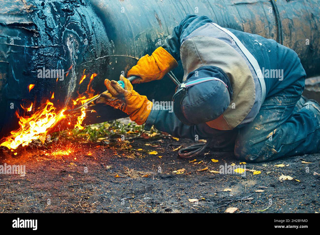 Der Schweißer arbeitet tagsüber mit Acetylenschweißen im Freien. Ein Arbeiter in Schutzkleidung schneidet ein Metallrohr zur Vergasung. Reparatur und Wartung der Gaspipeline. Stockfoto