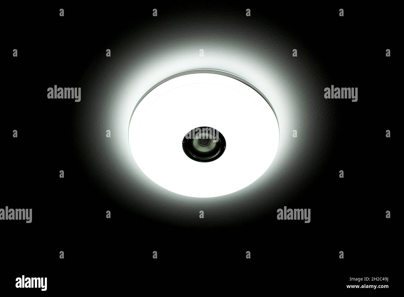 Weiße LED-Deckenleuchte mit integrierten kabellosen Lautsprechern auf schwarzem Hintergrund. Stockfoto