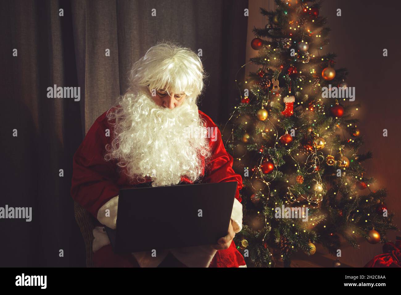 Der authentische Weihnachtsmann arbeitet an einem Laptop. Inneneinrichtung. In Erwartung von Weihnachten und Neujahr. Stockfoto