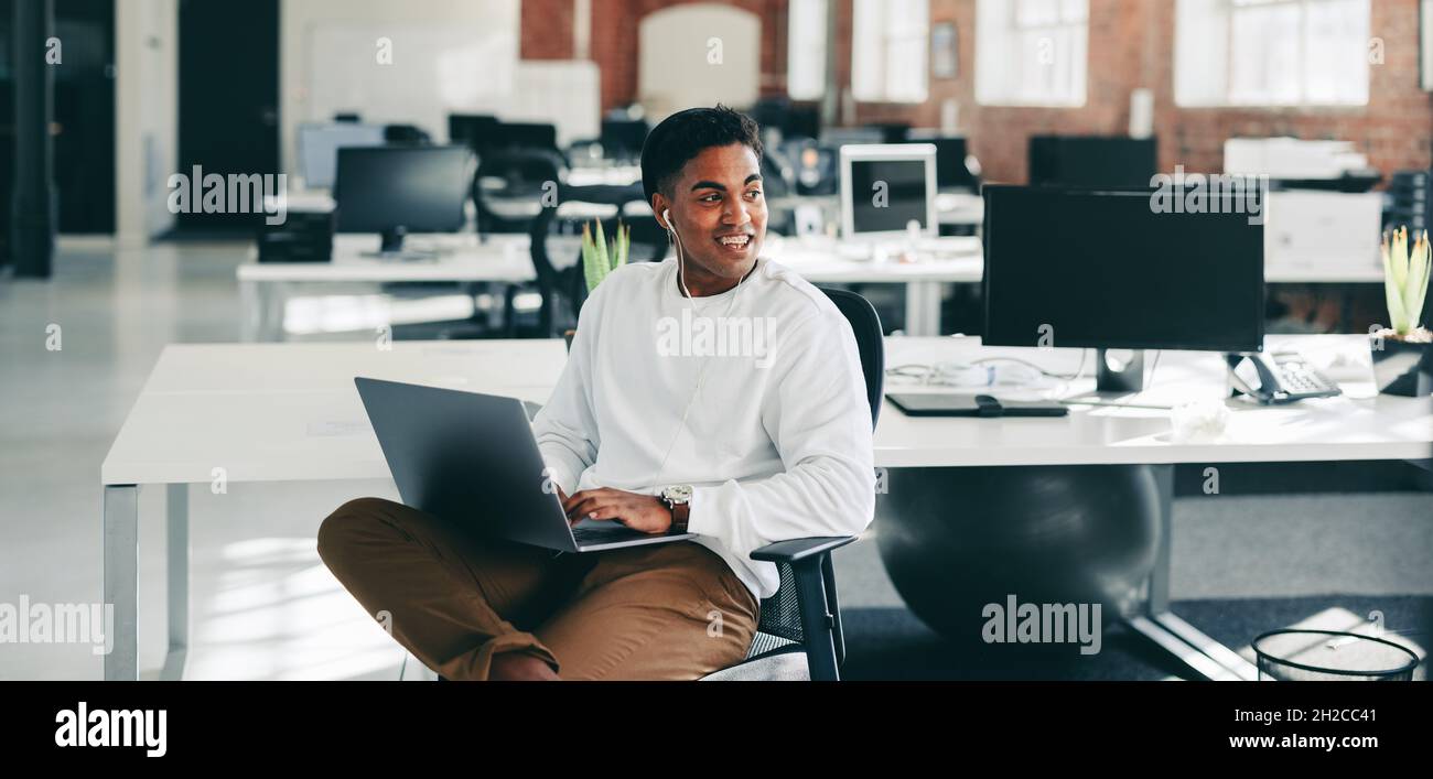 Junger Programmierer lächelt in einem modernen Büro. Ein glücklicher junger Geschäftsmann, der an einem modernen Arbeitsplatz auf einem Laptop arbeitet. Kreative Geschäftswelt Stockfoto