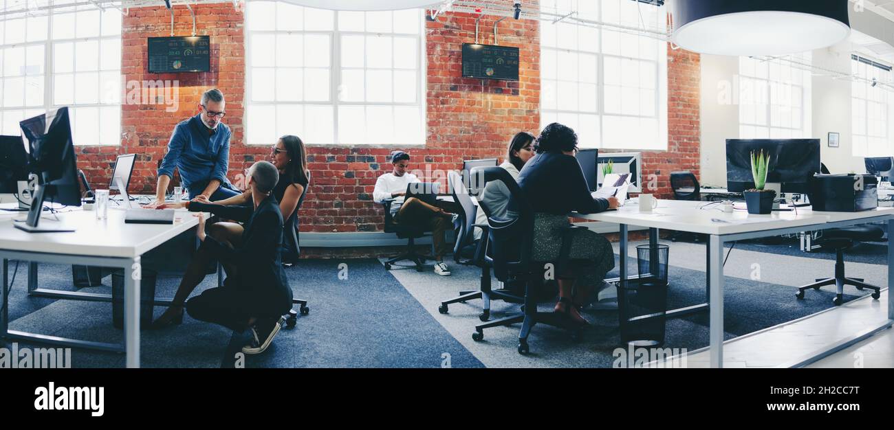 Kreative Geschäftsleute, die an einem modernen Arbeitsplatz zusammenarbeiten. Eine Gruppe von Geschäftsleuten, die an ihren Schreibtischen in einem Büro miteinander interagieren. Colle Stockfoto
