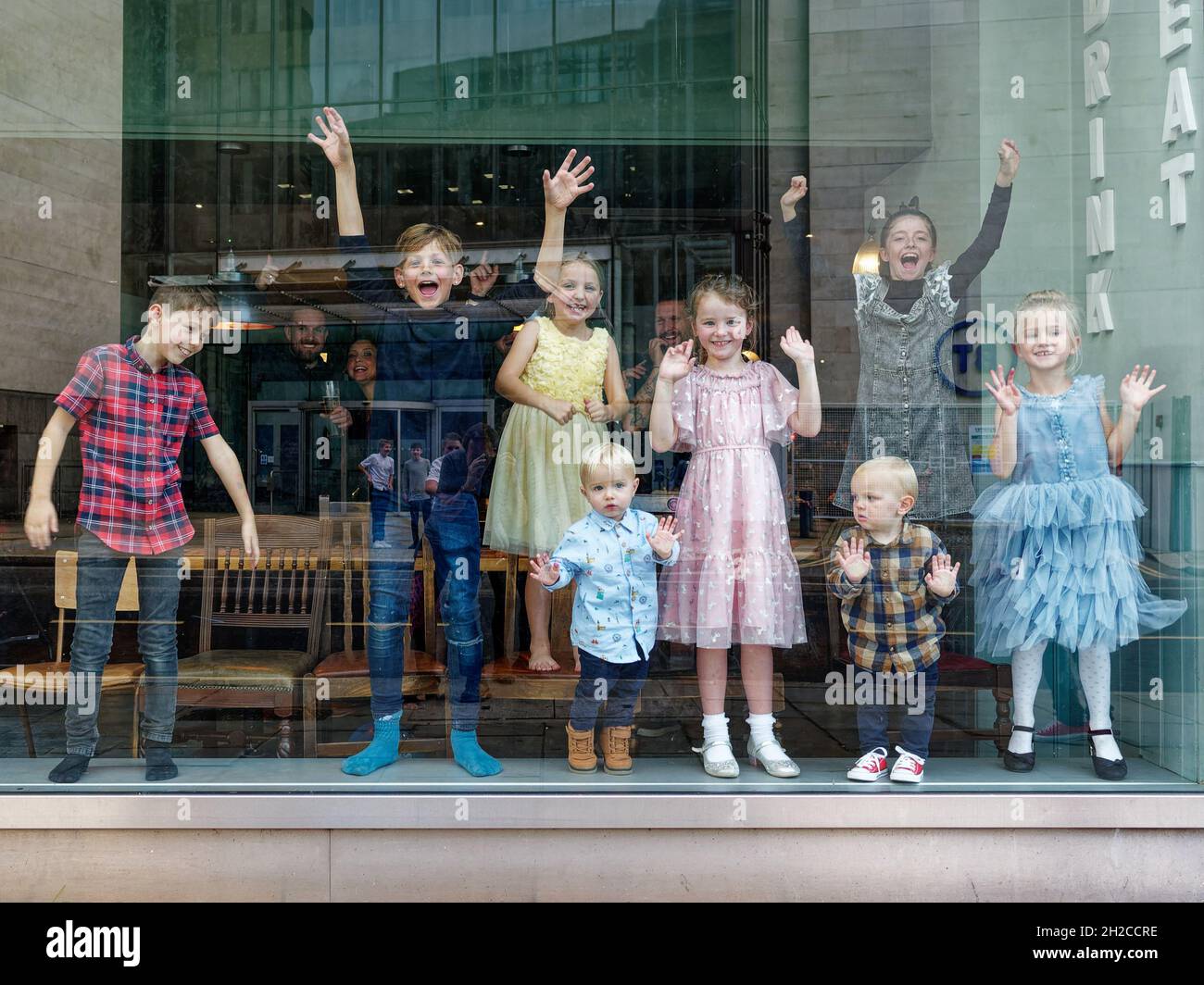 London, Greater London, England, Oktober 09 2021: Eine Gruppe von Kindern lächelt hinter einem Fenster, winkt und tanzt mit einem Roboter Stockfoto