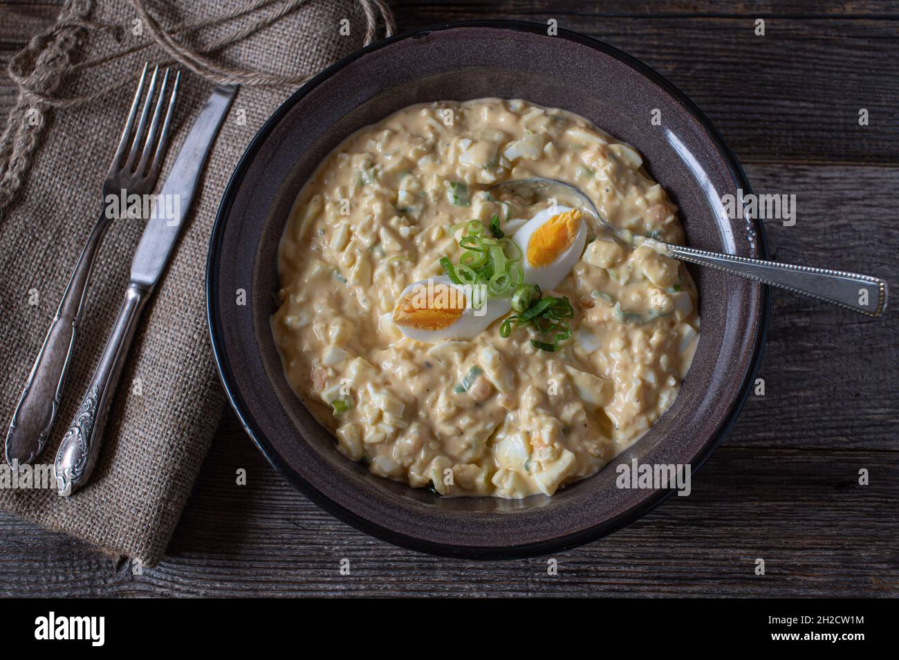 Eiersalat frisch und hausgemacht in einer braunen Emaille-Schüssel auf einem Holztisch Stockfoto