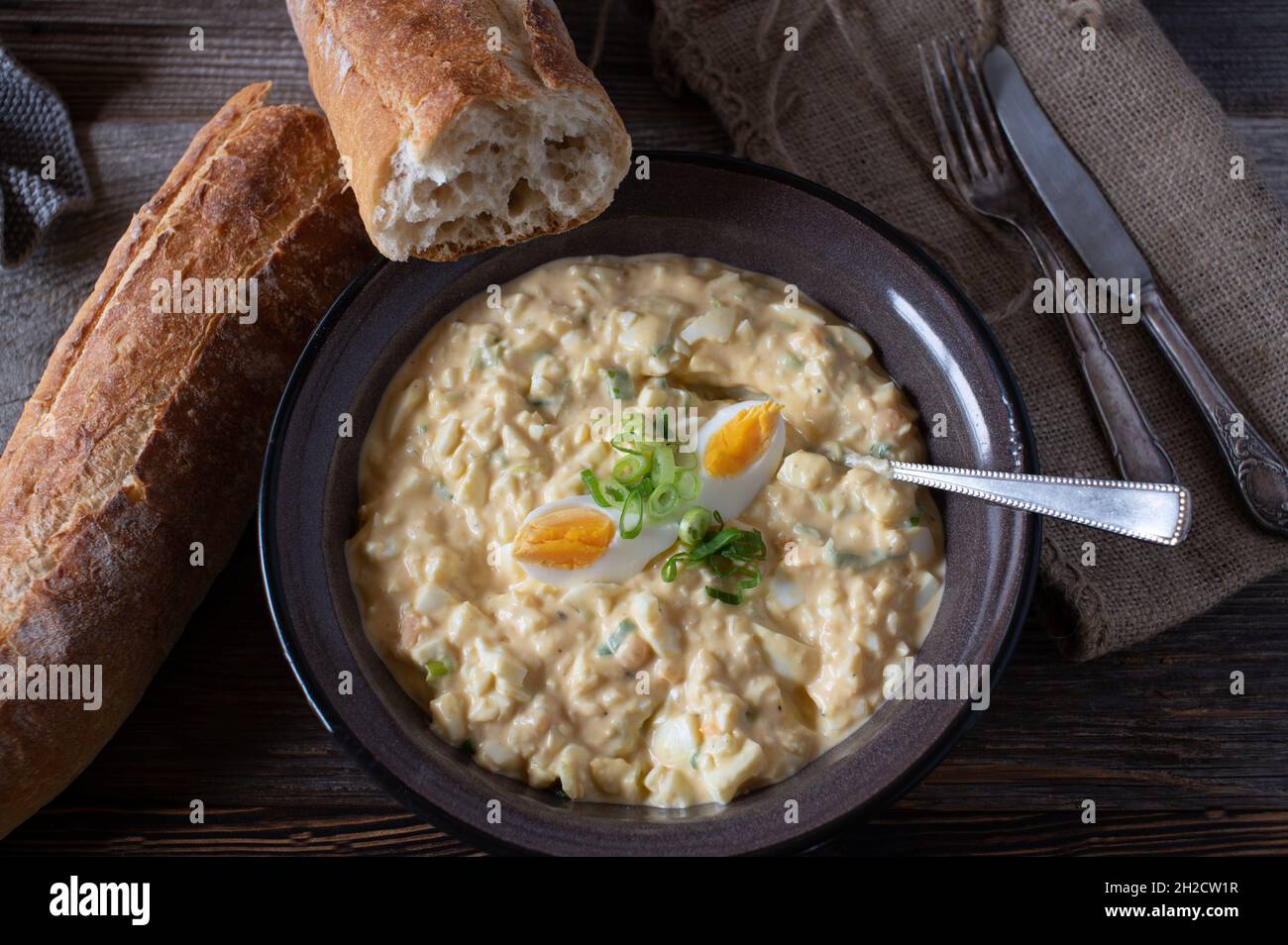 Eiersalat mit frischem Baguette auf einem Holztisch. Traditionelle hausgemachte Gerichte Stockfoto