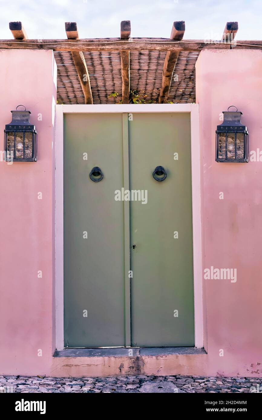 Grüne Tür. Isoliert. Vordertür mit Türknopfern und Außenlaternen an pinker Wand. Stockbild. Stockfoto