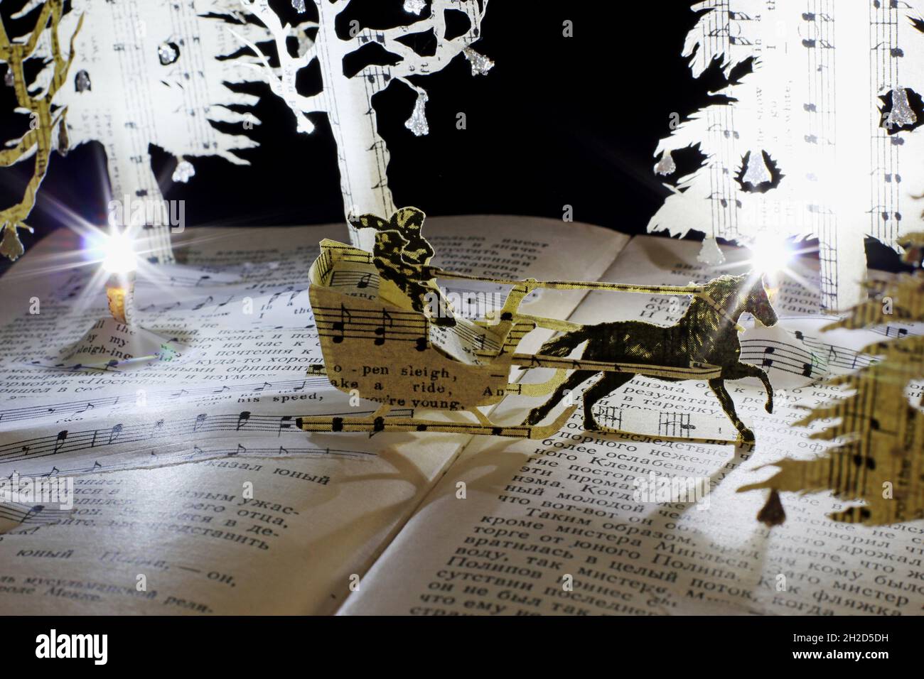 Handgefertigte Papierinterpretation von Jingle Bells als Buchskulptur-Szene. Ein Schlitten fährt durch ein magisches Winterwunderland. Stockfoto