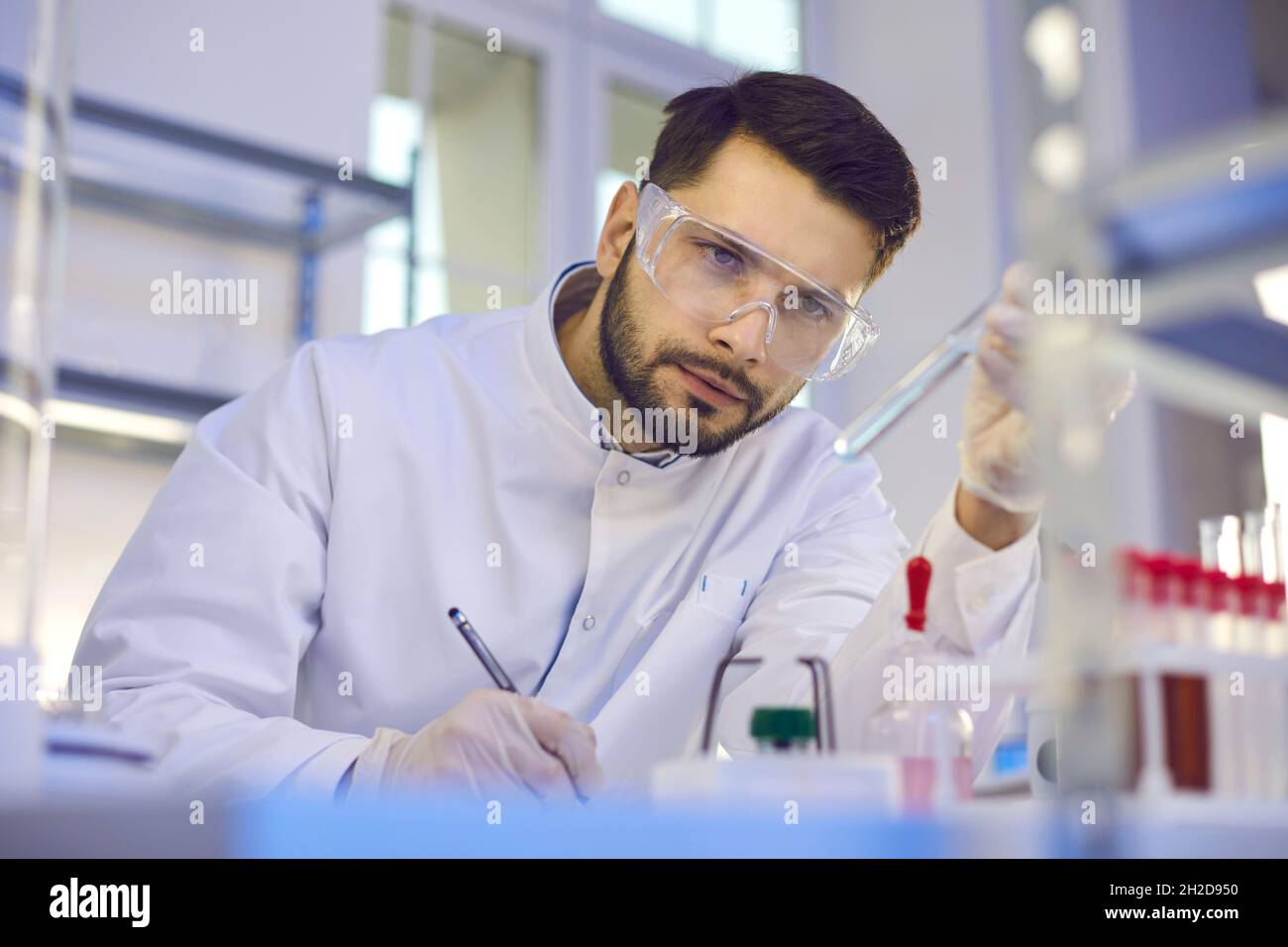 Ein Wissenschaftler betrachtet ein Reagenzglas mit Flüssigkeit in der Hand und zeichnet die Ergebnisse der Studie auf. Stockfoto