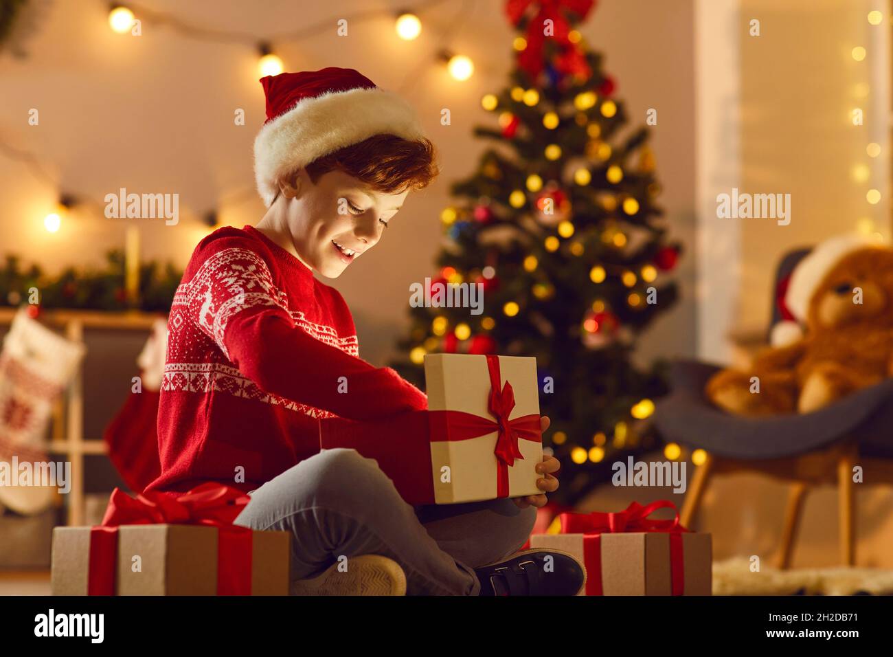 Happy aufgeregt Junge öffnet ein Weihnachtsgeschenk und aufgeregt schaut auf das magische Licht in der Box. Stockfoto