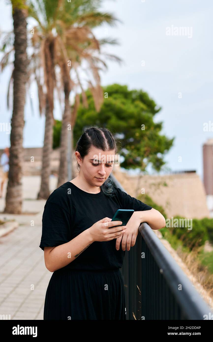 Frau in schwarzer Kleidung schaut in einem Park auf ihr Smartphone Stockfoto