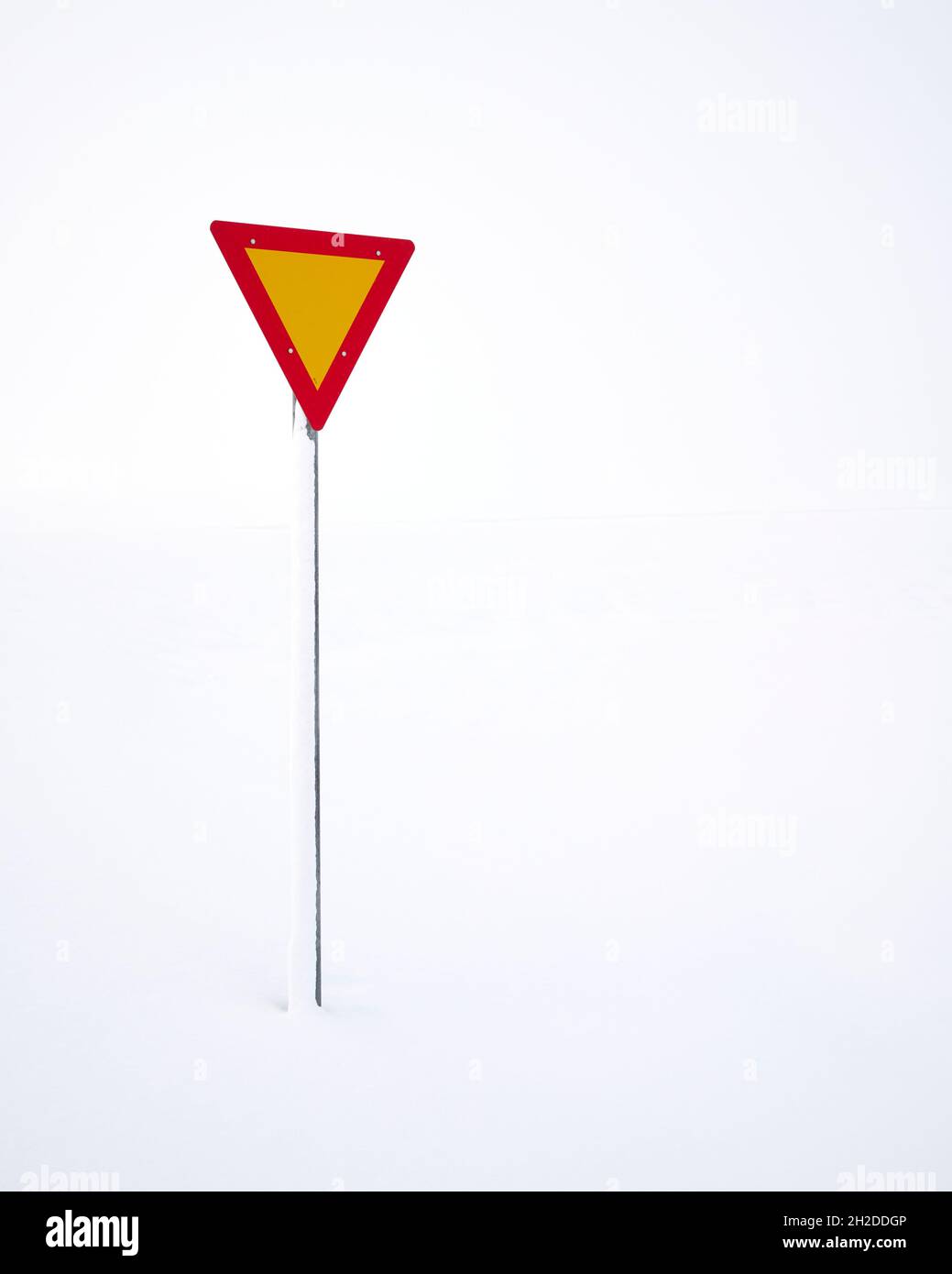 Give Way Schild mit roten und gelben Farben auf dem Postweg in verschneitem Gelände in Island Stockfoto