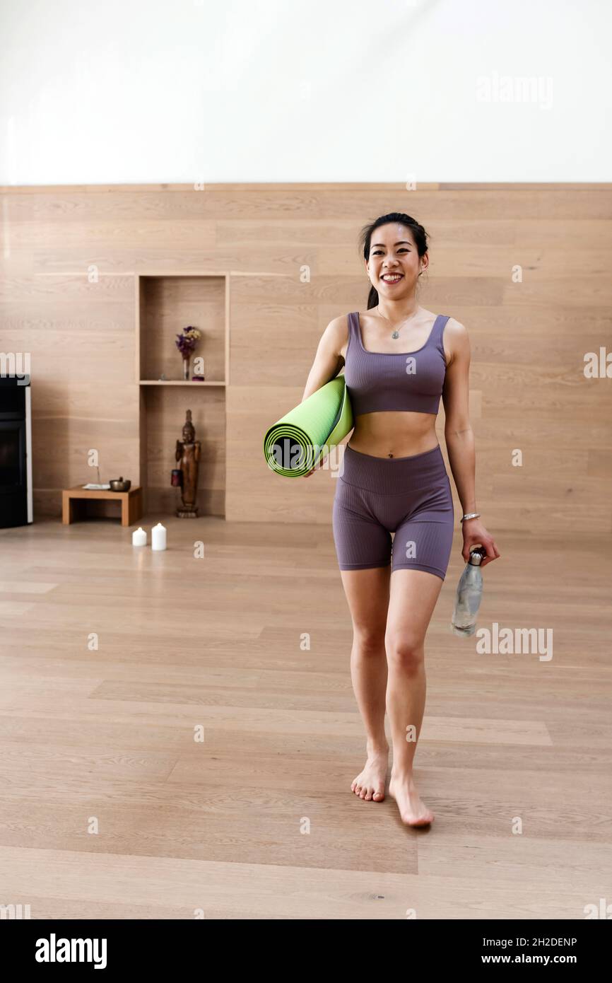 Asiatische Frau in Workout engen Anzug hält Yoga-Matte und Flasche Stockfoto