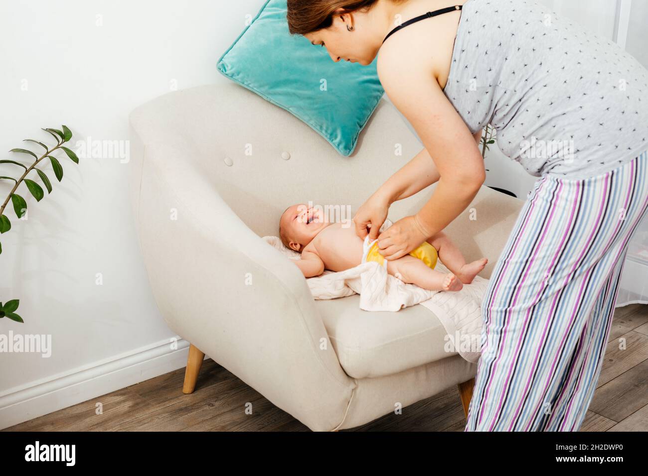 Mutter wechselt die wiederverwendbare Windel auf ihrem neugeborenen Baby auf dem Stuhl Stockfoto