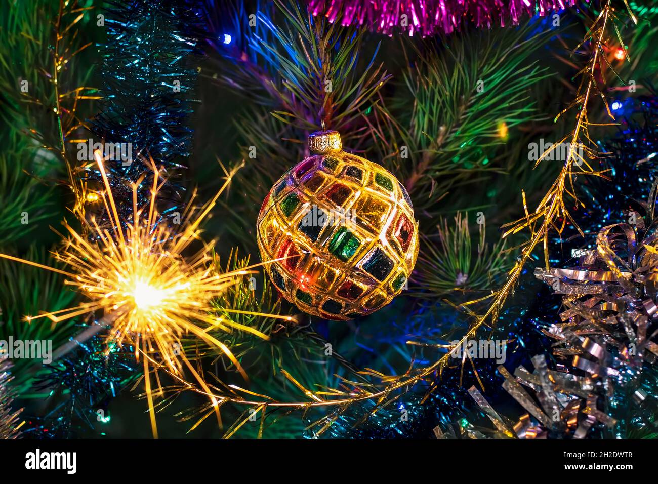 Weihnachten Neujahr Hintergrund. Eine bunte Kugel auf einem Weihnachtsbaum und ein brennender Funkler. Weihnachtsbaumschmuck mit einem glänzenden Ball und Glitzern Stockfoto