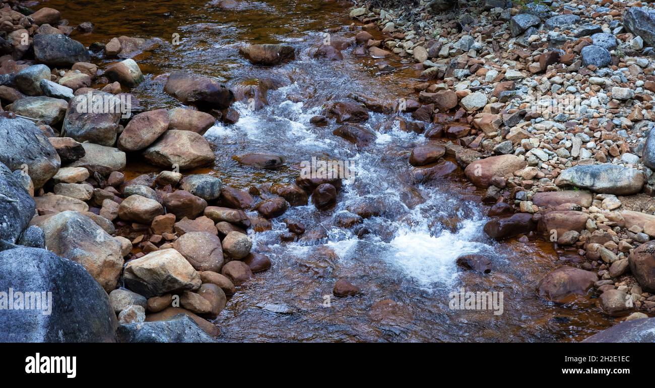 Wasser fließt den Fluss entlang um Felsen herum. Stockfoto
