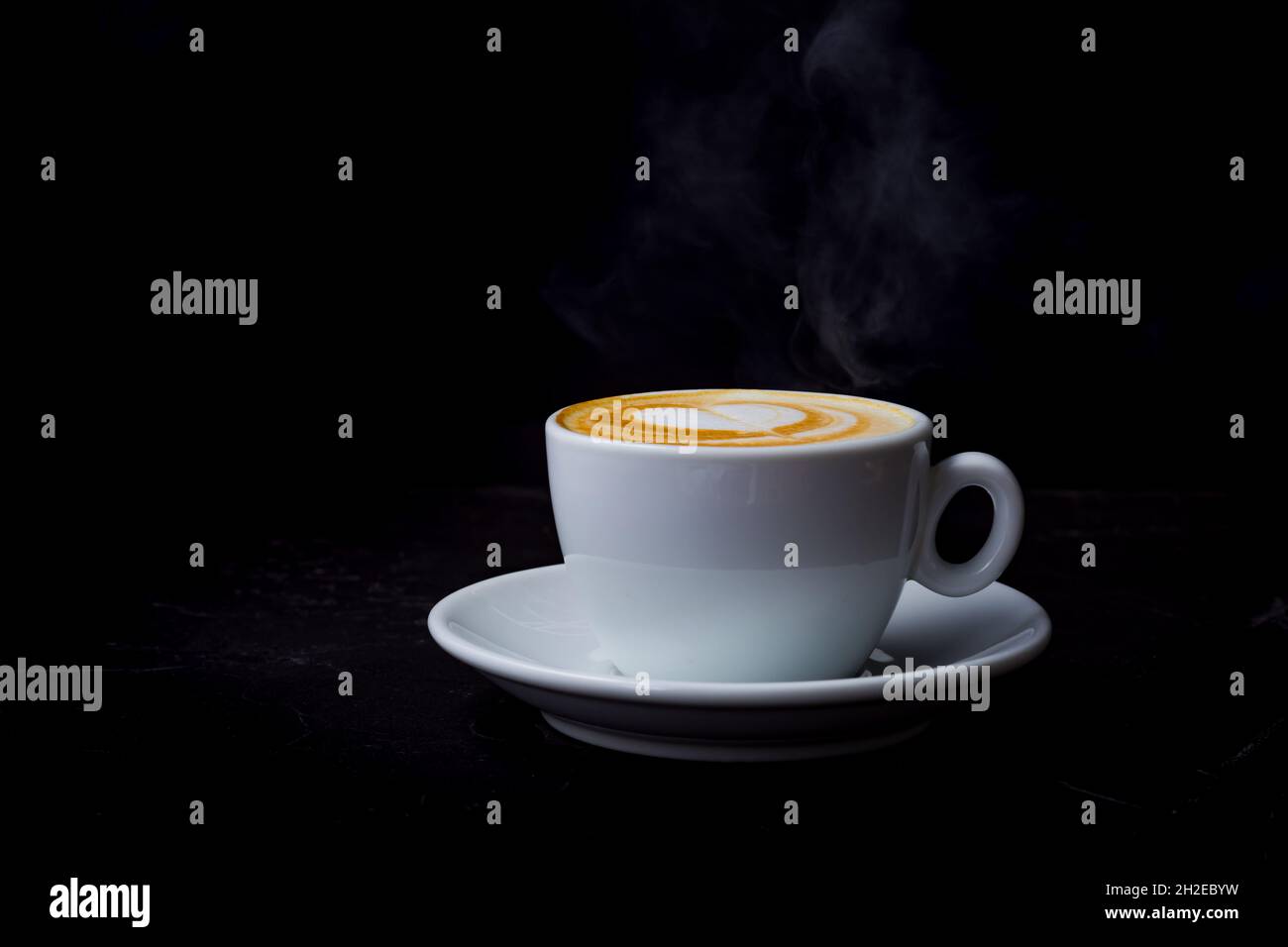 Cappuccino mit Dampf in weißer Tasse auf schwarzem Hintergrund Stockfoto