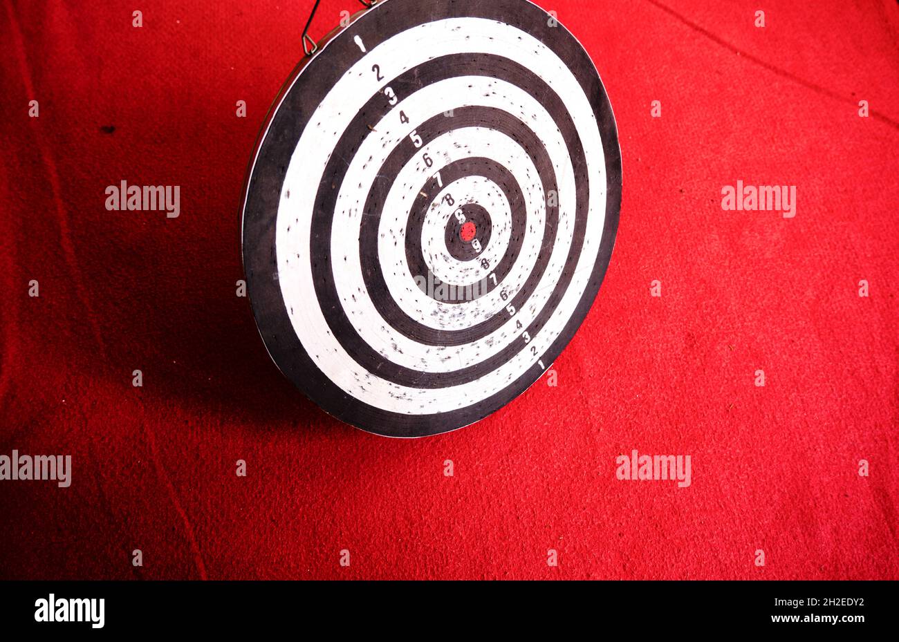 Gebrauchte Dartscheibe, die auf rotem Teppich und seinen Schatten steht. Stockfoto
