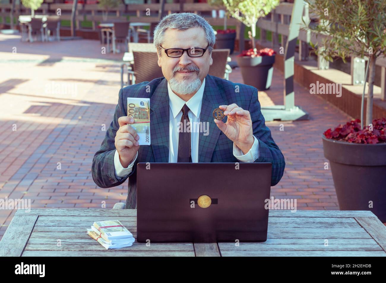 Der Finanzmann hält Geld in den Händen und Bitcoins. Mit seinem Laptop, der an der Börse gehandelt wurde, machte er Geld. Stockfoto