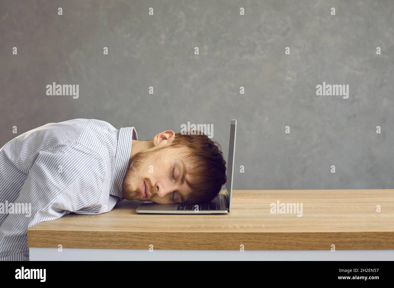 Müder Büroangestellter, der an einem Schreibtisch sitzt und seinen Kopf auf eine Laptop-Tastatur legt, schläft. Stockfoto