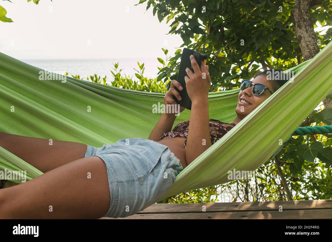 Schöne dunkelhäutige Frau liest in einer Hängematte am Meer Stockfoto
