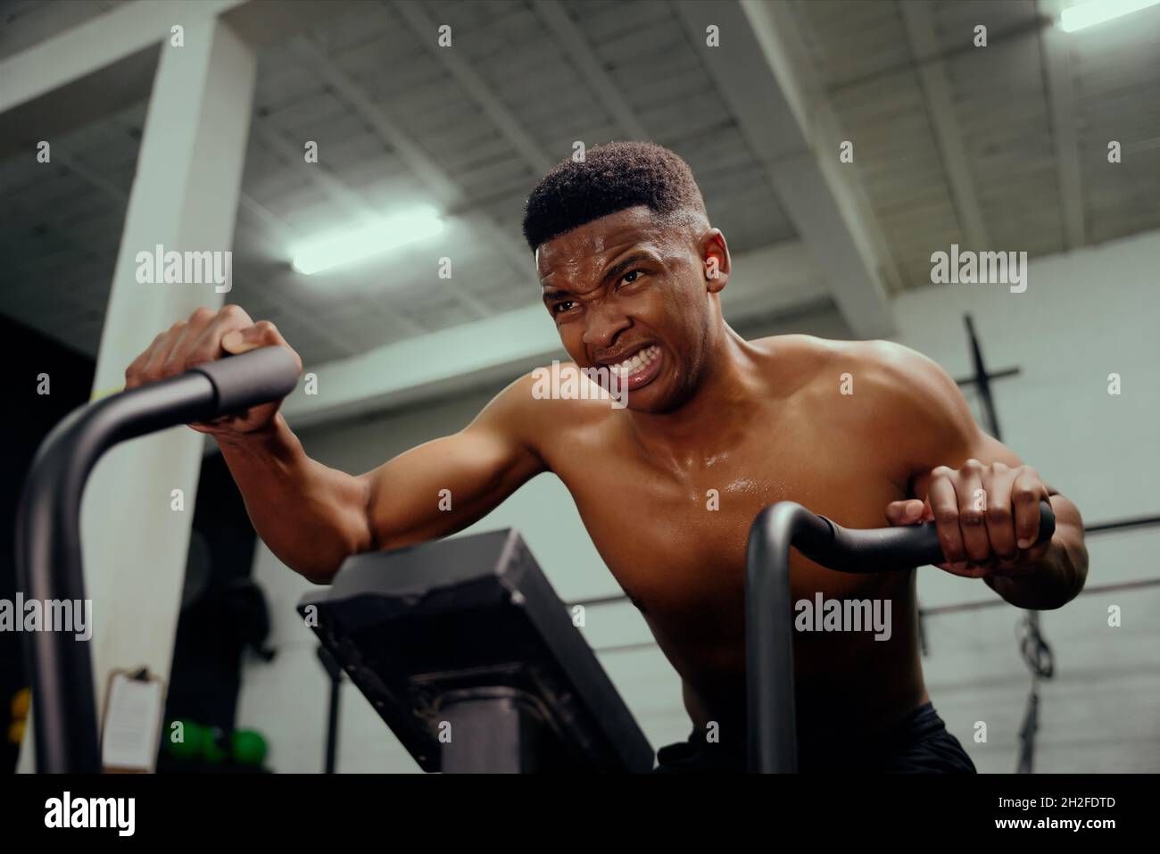 Afroamerikanischer Mann mit einem Ellipsentrainer, der intensives Training macht. Männlicher Athlet, der intensiv im Fitnessstudio trainiert. Hochwertige Fotos Stockfoto