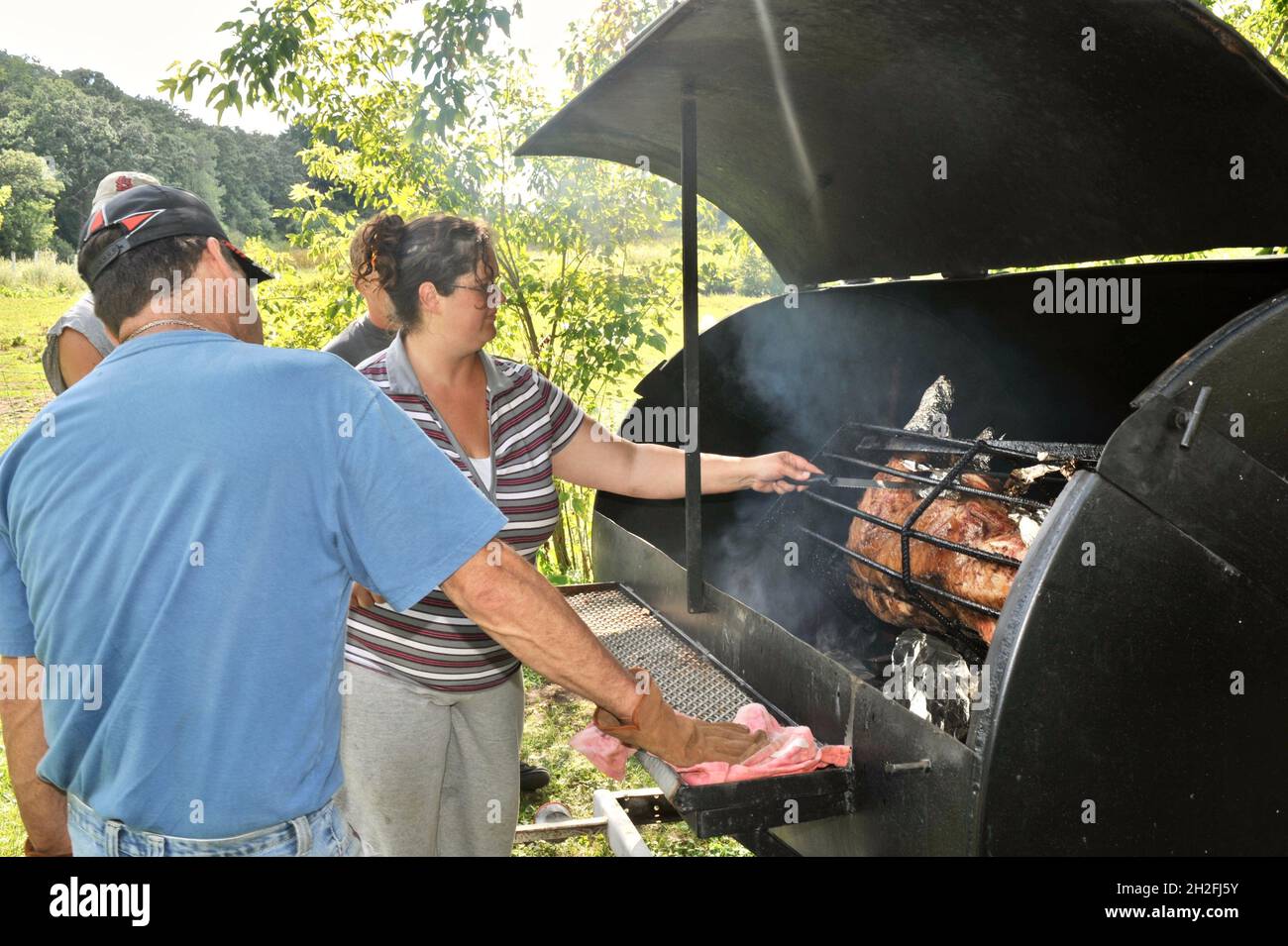 Zubereitung und Spieß-Rösten von ganzen Schwein draußen auf einem Grill, über Holzkohle, auf einer Farm im Mittleren Westen, Blanchardville, Wisconsin, USA Stockfoto