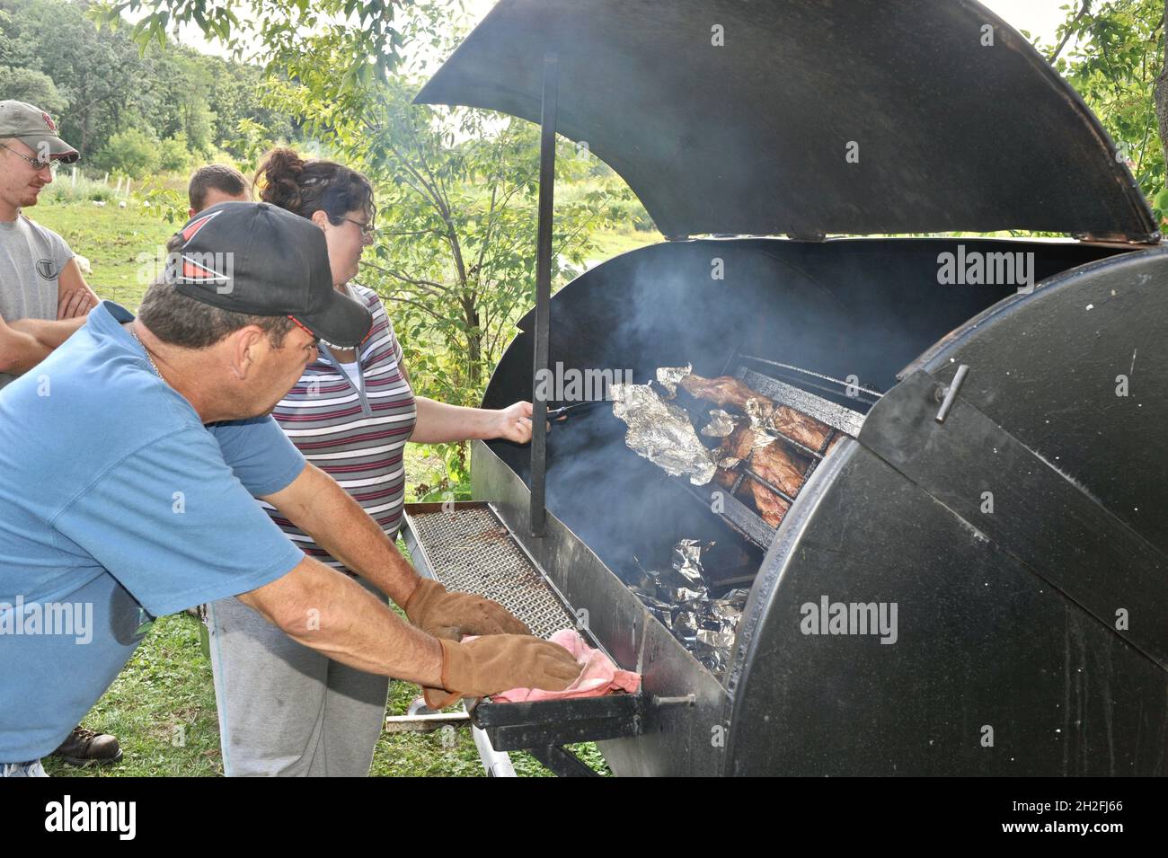 Zubereitung und Spieß-Rösten von ganzen Schwein draußen auf einem Grill, über Holzkohle, auf einer Farm im Mittleren Westen, Blanchardville, Wisconsin, USA Stockfoto