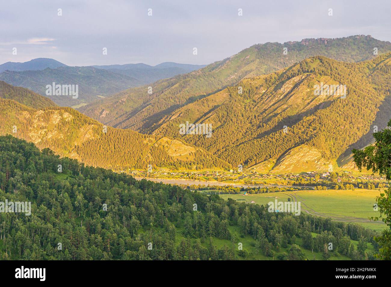 Ein Blick vom Berg auf die Siedlung im Tal des Zusammenflusses von Bergflüssen bei Sonnenuntergang oder Sonnenaufgang Stockfoto