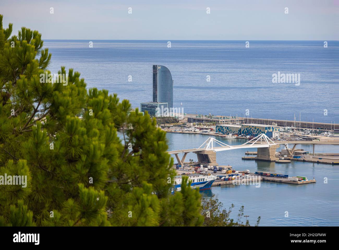 Barcelona, Spanien - 22. September 2021: Blick durch die Bäume vom Park Güell über die Stadt und das neue Architekturdenkmal, das luxuriöse Hotel W, Stockfoto
