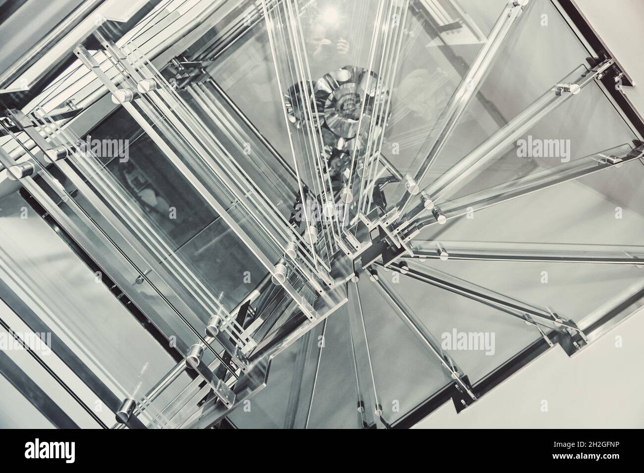 Moderne Wendeltreppe aus Metall mit Stufen aus durchsichtigen Glas, die in einem geräumigen Lichtsaal in der Nähe der Unterseite des Gebäudes installiert ist Stockfoto