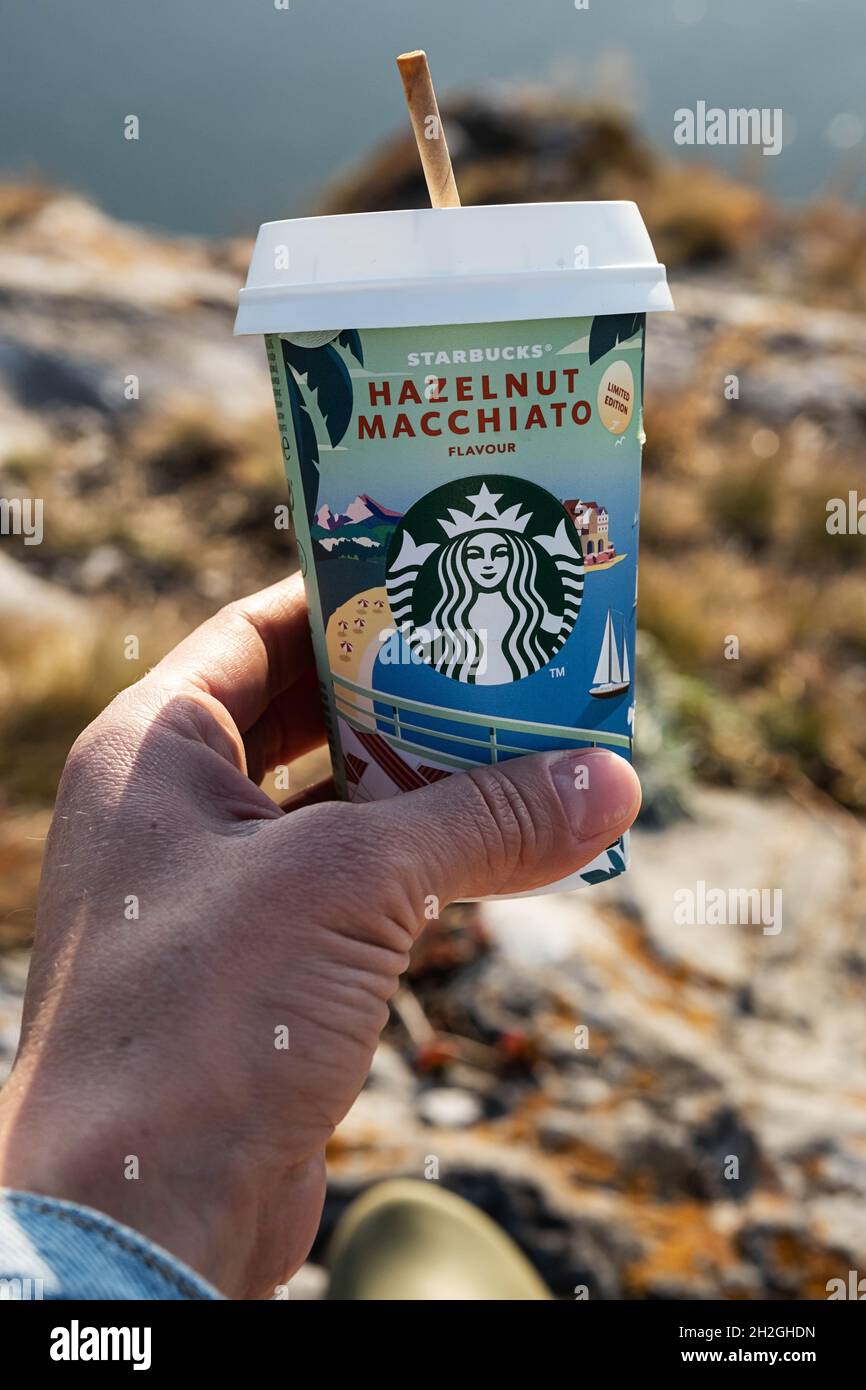 Kemerowo, Russland - 17. Oktober 2021: Frau hält Starbucks-Kaffee auf landschaftlichem Hintergrund. Haselnuss Macchiato to go Kaffeetasse, Nahaufnahme. Stockfoto