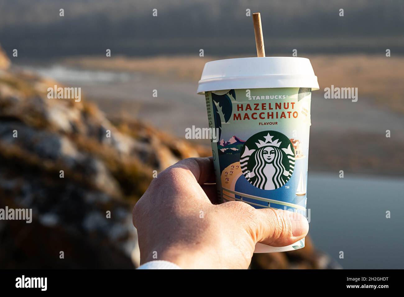 Kemerowo, Russland - 17. Oktober 2021: Frau hält Starbucks-Kaffee auf landschaftlichem Hintergrund. Haselnuss Macchiato to go Kaffeetasse, Nahaufnahme. Stockfoto