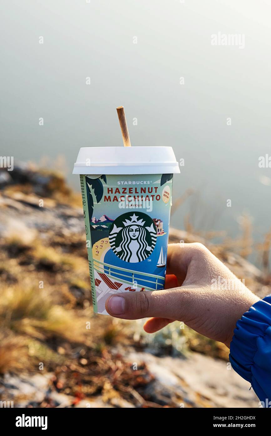 Kemerowo, Russland - 17. Oktober 2021: Mann hält Starbucks-Kaffee auf landschaftlichem Hintergrund. Haselnuss Macchiato to go Kaffeetasse, Nahaufnahme. Stockfoto